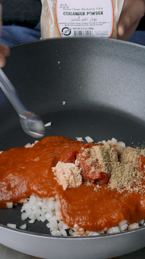 Next add diced onion, tomato sauce, tomato paste, minced garlic, turmeric, and coriander to a large pan. 